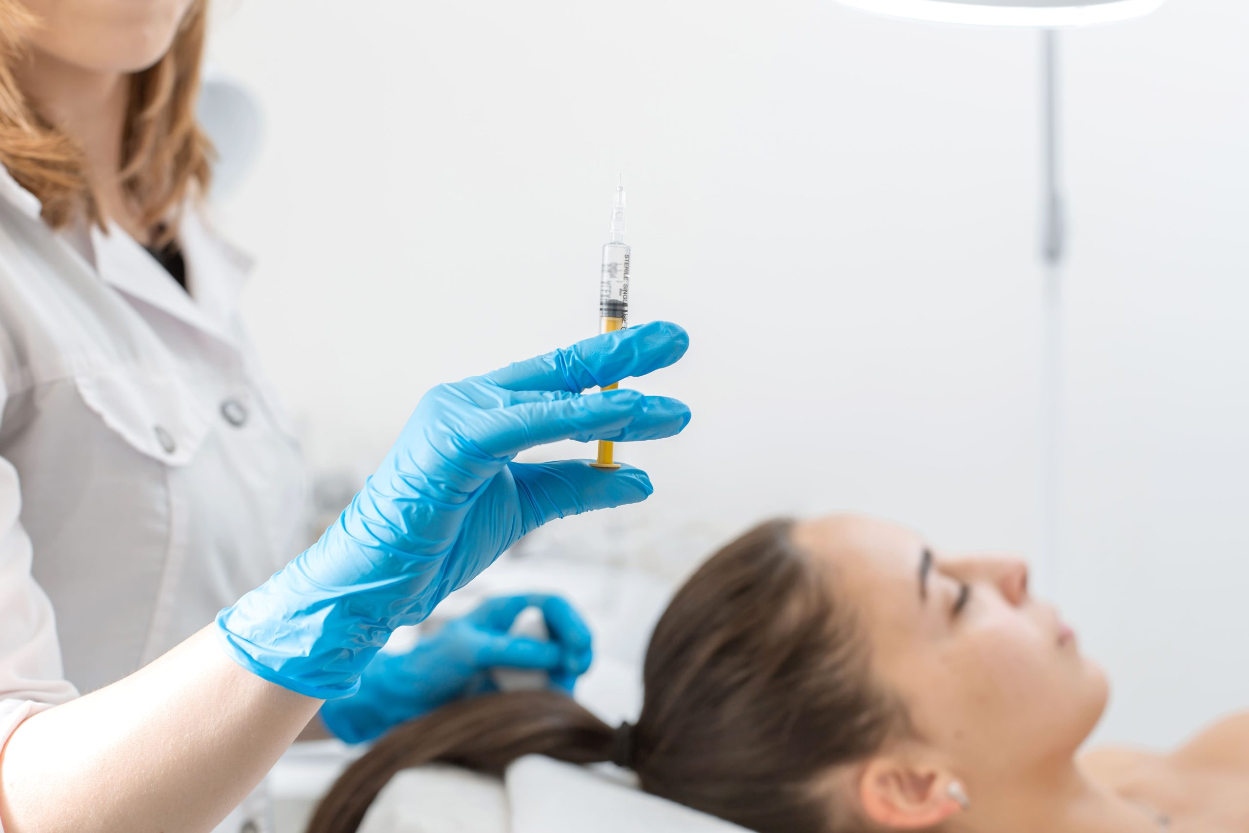 Profissional com uma seringa na mão para aplicar no couro cabeludo da paciente. Tratamento de exossomos capilares