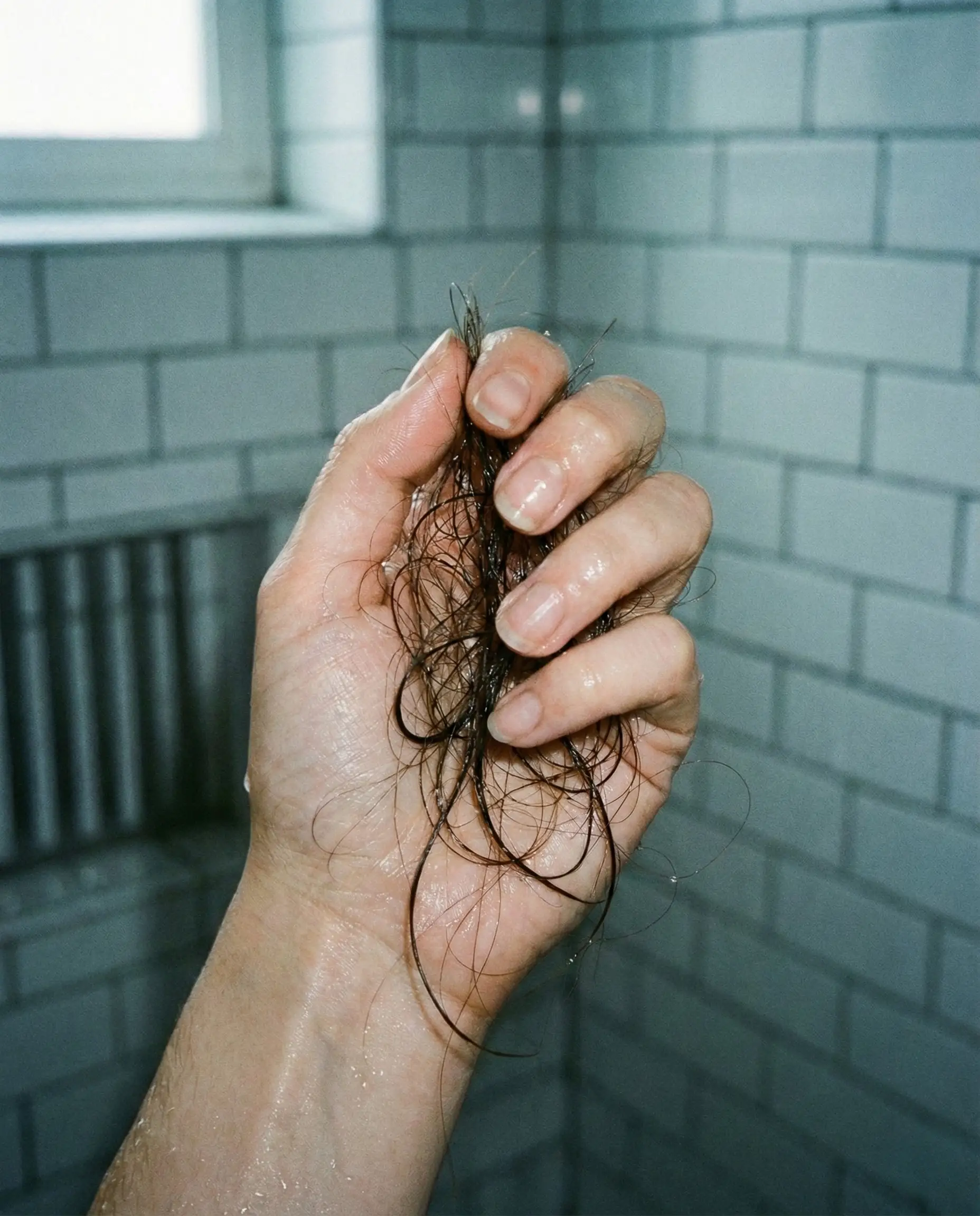 Mulher no banheiro olhando no espelho e puxando mecha de cabelo ralo com expressão de tristeza. Representa a frustração da queda de cabelo persistente que necessita de fototerapia e bioestimulação.