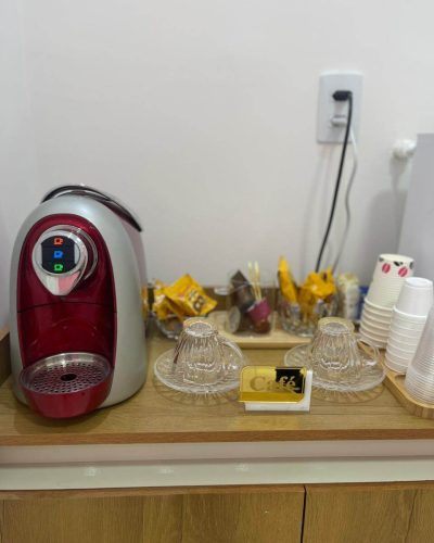 Mesa de Café na Recepção com máquina de café expresso, xicaras, copos descartáveis e biscoitos.
