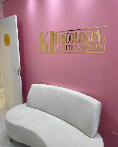 Sala de recepção da Clínica de Estética Dra. Karen Lima mostrando um sofá, onde os pacientes podem esperar confortavelmente pelo seu atendimento. Logo acima do sofá esta o logotipo da clínica KL Tricologia e Estética Avançada
